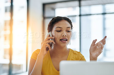 Buy stock photo Shot of a young designer talking on a cellphone while working on a laptop in an office
