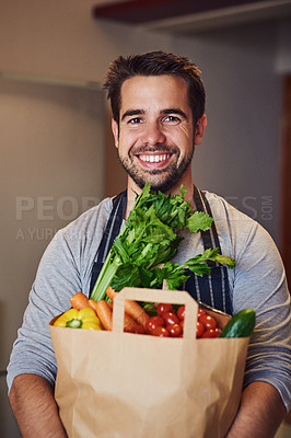 Buy stock photo Portrait of a happy young man posing with a bag of groceries in his kitchen at home