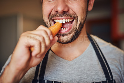 Buy stock photo Cropped shot of an unidentifiable young man eating a carrot in his kitchen at home