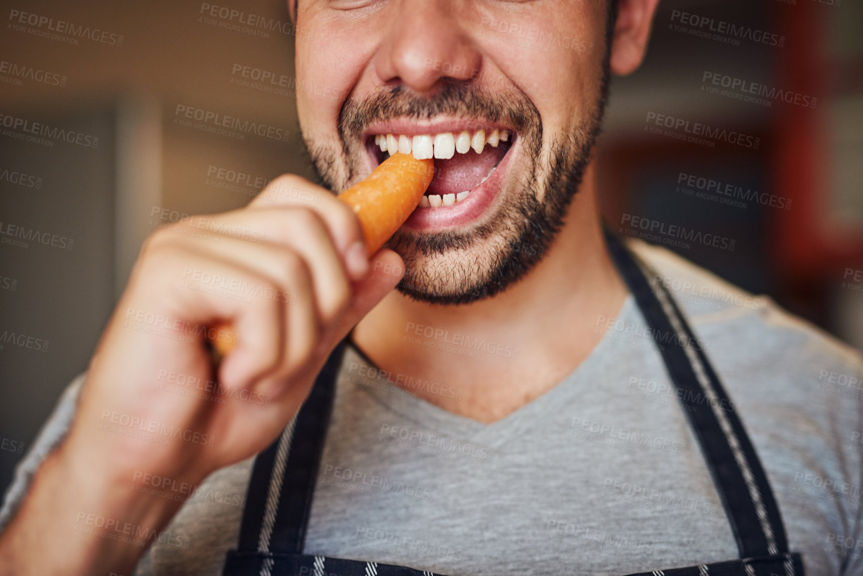 Buy stock photo Cropped shot of an unidentifiable young man eating a carrot in his kitchen at home