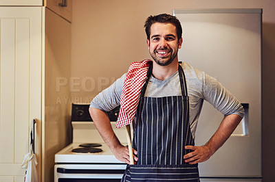 Buy stock photo Portrait of a happy young man wearing an apron while standing in his kitchen at home