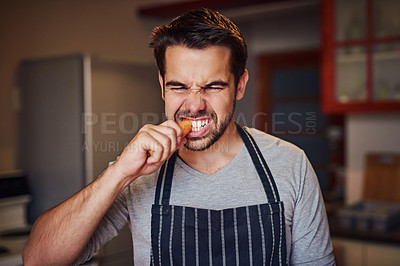 Buy stock photo Shot of a happy young man eating a carrot while standing in his kitchen at home