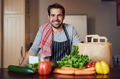 Buy stock photo Portrait of a happy young man posing behind a selection of fresh ingredients in his kitchen