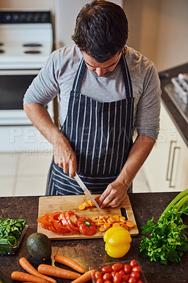 Buy stock photo High angle shot of an unidentifiable young man chopping vegetables in his kitchen at home
