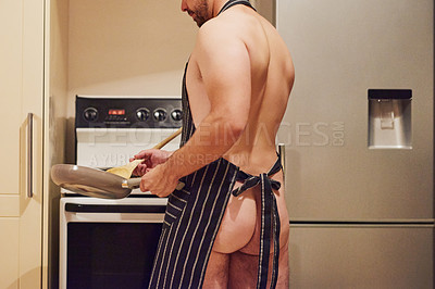 Buy stock photo Rearview shot of an unidentifiable young man wearing only an apron while cooking in his kitchen at home