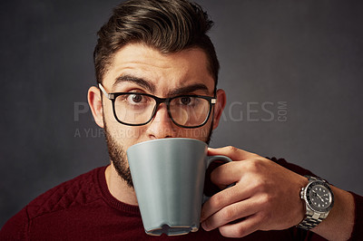 Buy stock photo Studio portrait of a handsome young man drinking coffee against a dark background