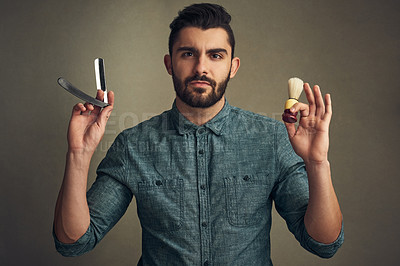 Buy stock photo Studio shot of a handsome young man holding a straight razor and a shaving brush in his hands