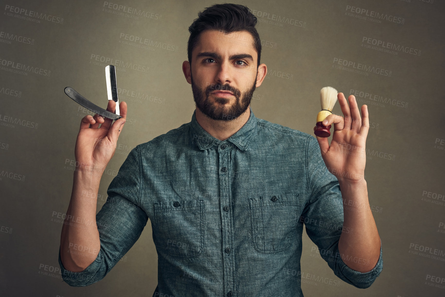 Buy stock photo Studio shot of a handsome young man holding a straight razor and a shaving brush in his hands