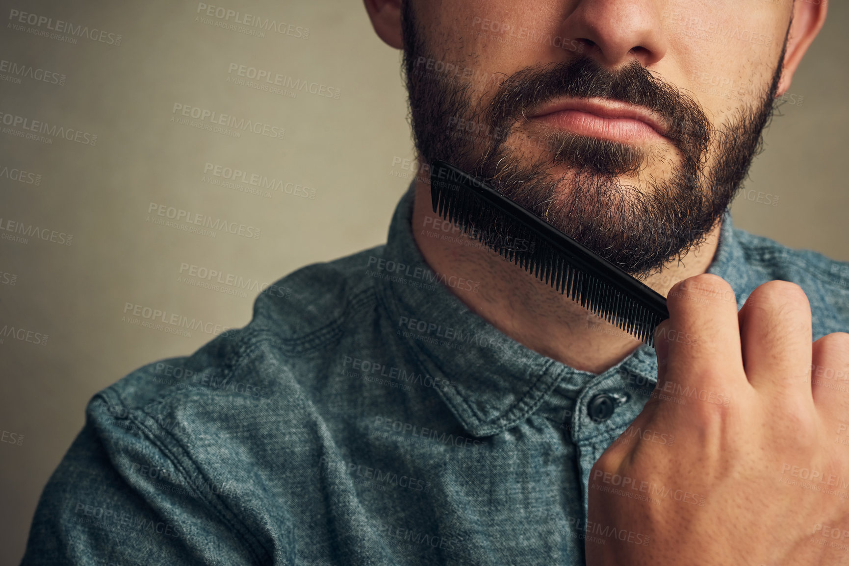 Buy stock photo Cropped shot of a handsome young man combing his beard against a grey background