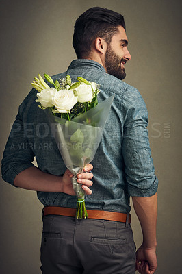 Buy stock photo Studio shot of a handsome young man holding a bunch of flowers behind his back