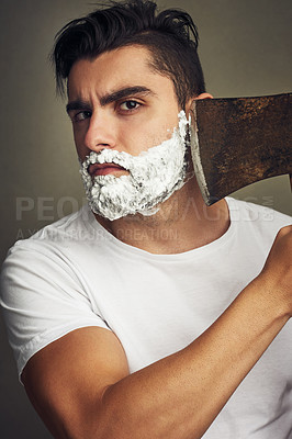 Buy stock photo Shot of a handsome young man shaving his beard with a lumberjack
