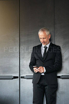 Buy stock photo Cropped shot of a handsome mature businessman standing and texting on his cellphone in the office