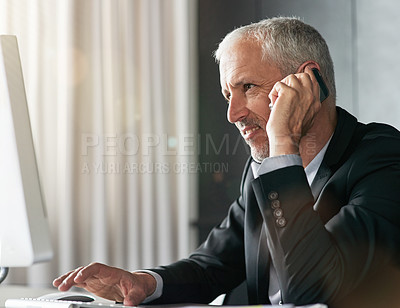 Buy stock photo Cropped shot of a handsome mature businessman sitting in the office in front of the computer while on his phone