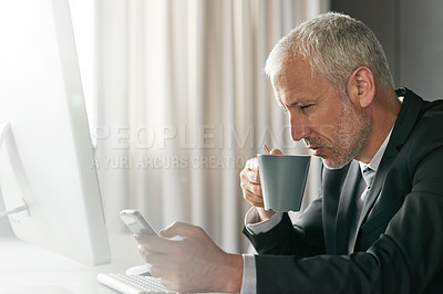 Buy stock photo Cropped shot of a handsome mature businessman sitting in the office using his phone and drinking a cup of coffee