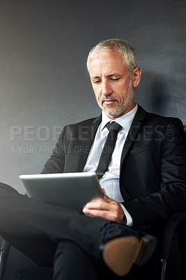 Buy stock photo Cropped shot of a handsome mature businessman sitting in the office and working on his tablet