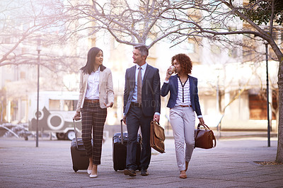 Buy stock photo Shot of a group of business people walking and talking to each other while carrying their luggage outside