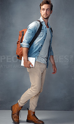 Buy stock photo Shot of a handsome young man  with a backpack holding a tablet while standing in the studio