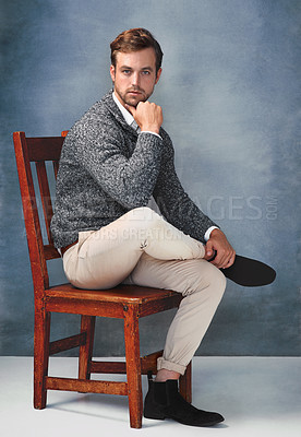 Buy stock photo Portrait of a handsome young man posing on a chair against a gray background in the studio