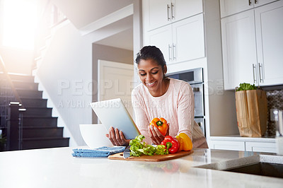 Buy stock photo Shot of a young woman using a digital tablet while preparing a healthy meal at home