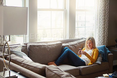 Buy stock photo Shot of a young woman using her cellphone while relaxing in her living room