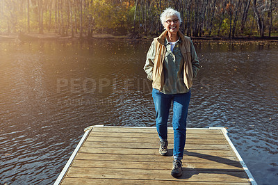 Buy stock photo Shot of a senior woman going for a walk on a jetty next to a lake