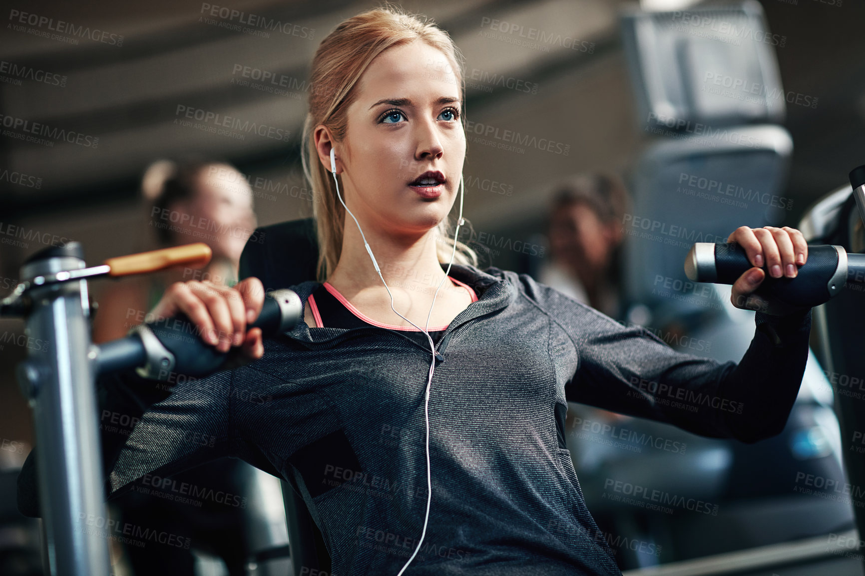 Buy stock photo Gym, woman and serious on chest press machine for workout to exercise for health, fitness and muscles. Female person, committed and earphones with training for wellbeing, wellness and self care