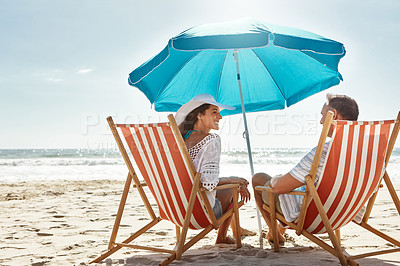 Buy stock photo Shot of a mature couple relaxing together on deck chairs at the beach