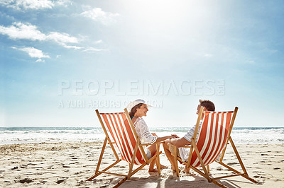 Buy stock photo Shot of a mature couple relaxing together on deck chairs at the beach