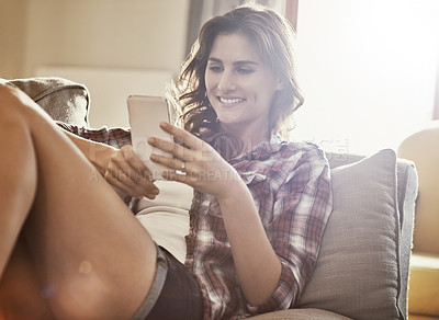 Buy stock photo Shot of a young woman relaxing on the sofa at home and using a mobile phone