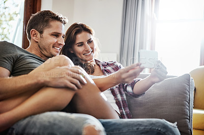 Buy stock photo Shot of a young couple relaxing on the sofa and taking selfies on a mobile phone