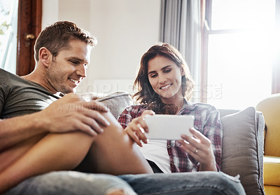 Buy stock photo Shot of a young couple relaxing on the sofa together and using a mobile phone