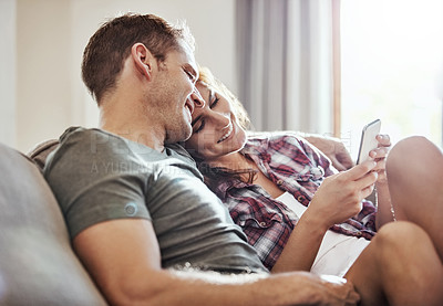 Buy stock photo Shot of a young couple relaxing on the sofa together and using a mobile phone