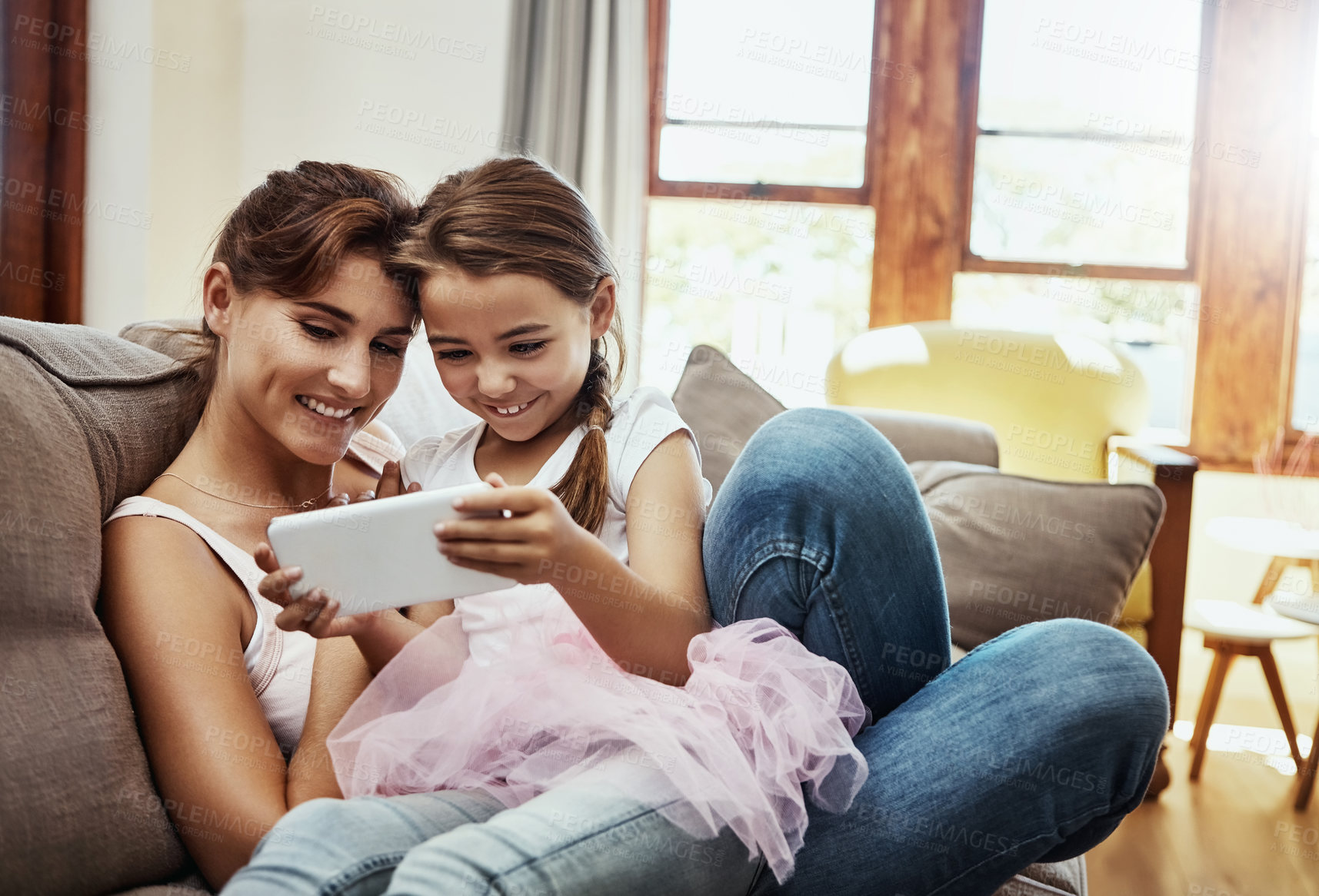 Buy stock photo Shot of a little girl using a cellphone while bonding with her mother at home