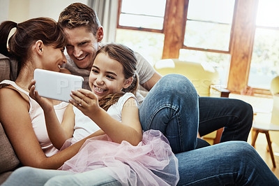 Buy stock photo Shot of a little girl using a cellphone while bonding with her family at home
