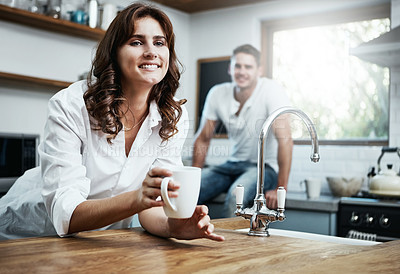 Buy stock photo Shot of a young woman drinking coffee with her husband in the background at home