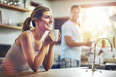 Buy stock photo Shot of a young woman having her morning coffee with her boyfriend standing in the background
