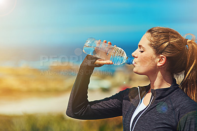 Buy stock photo Shot of a sporty young woman drinking water outdoors