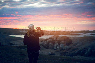Buy stock photo Shot of an unrecognizable woman taking a picture of the sunset outdoors