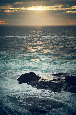Buy stock photo Shot of ocean waves crashing against boulders on the seashore outdoors