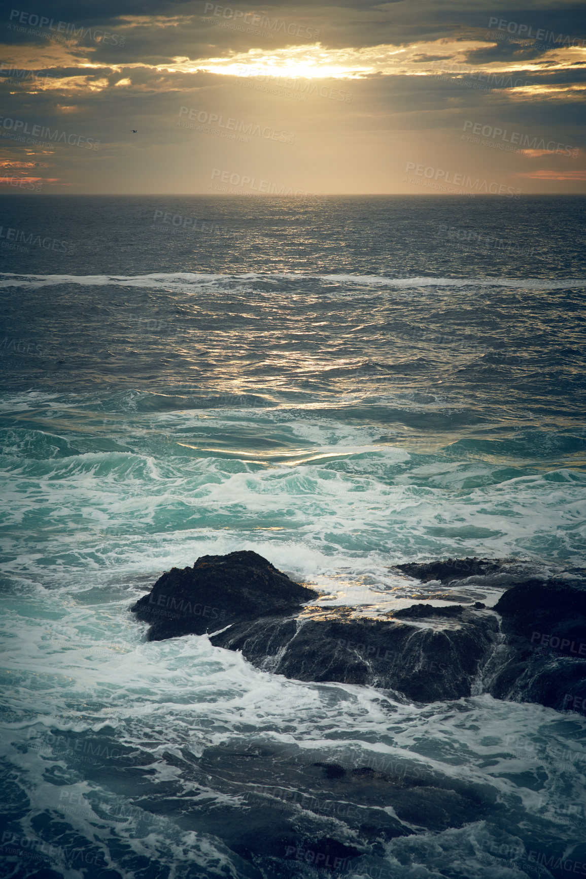 Buy stock photo Shot of ocean waves crashing against boulders on the seashore outdoors