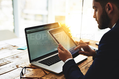 Buy stock photo Cropped shot of a young businessman using a digital tablet and laptop at his work desk