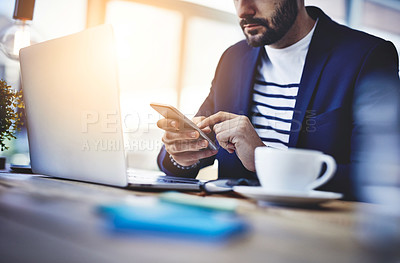 Buy stock photo Cropped shot of a young businessman using a mobile phone and laptop at his work desk