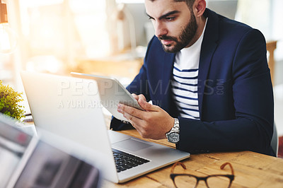 Buy stock photo Cropped shot of a young businessman using a digital tablet and laptop at his work desk