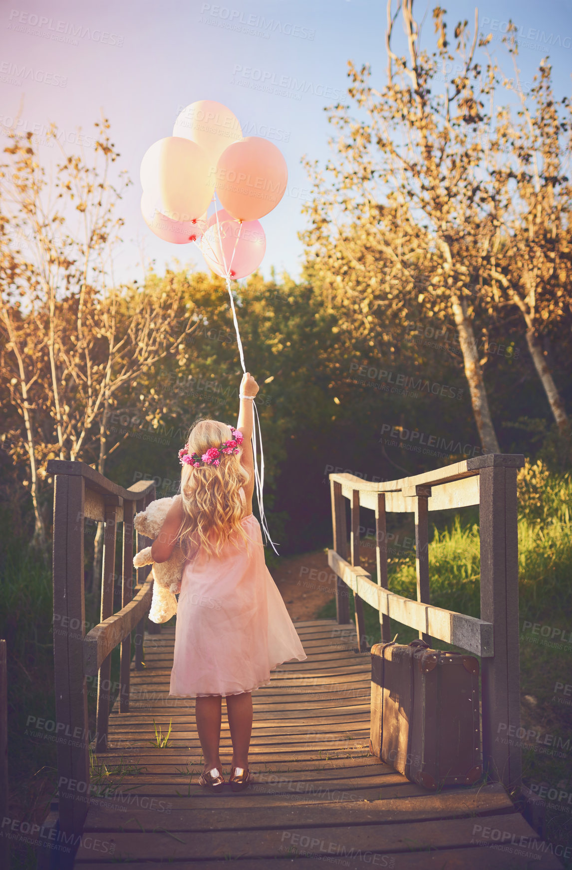 Buy stock photo Shot of a unrecognizable little girl holding balloons and a teddy bear while standing in the middle of a bridge