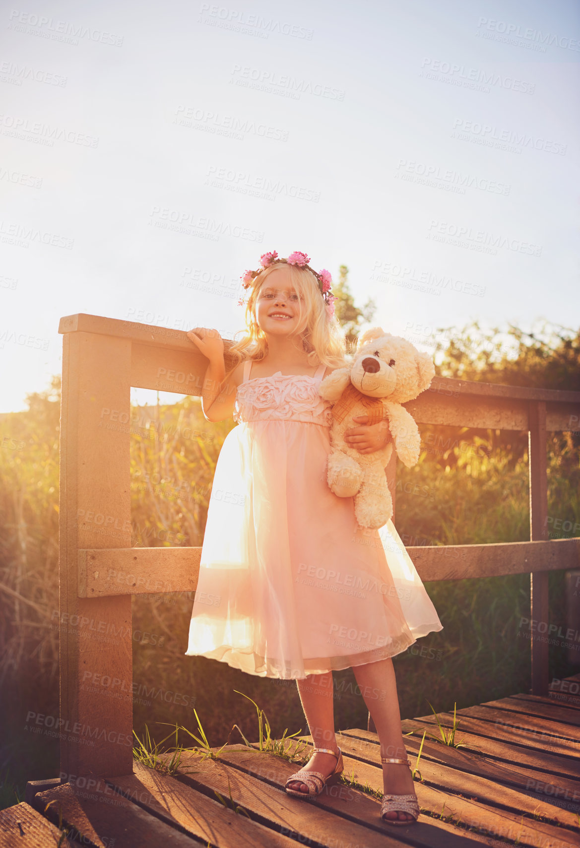 Buy stock photo Shot of a happy little girl holding a teddy bear and looking at the camera while standing on a bridge