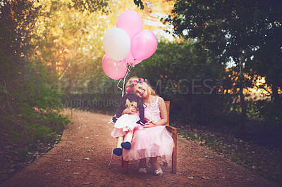 Buy stock photo Shot of a happy little girl sitting and waiting with a doll and balloons in the middle of a dirt road