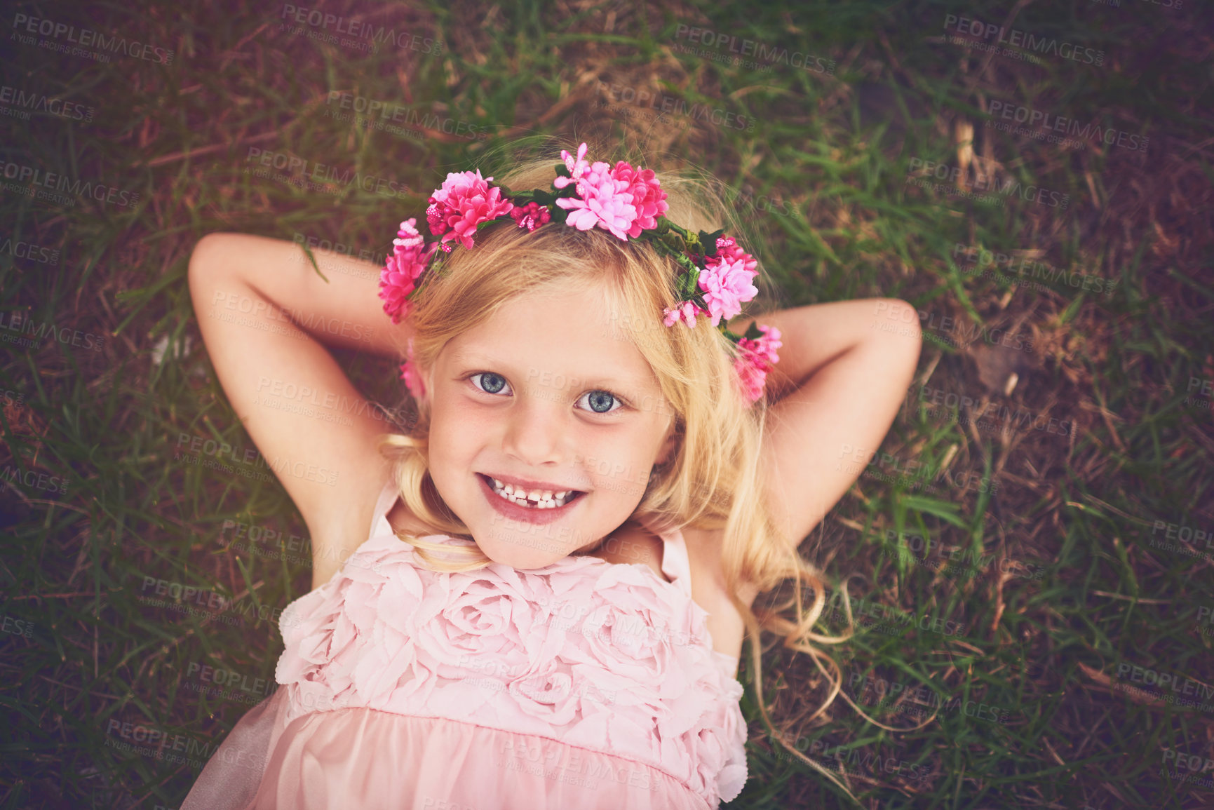 Buy stock photo Shot of a happy little girl looking at the camera while lying on the grass and relaxing outside in nature