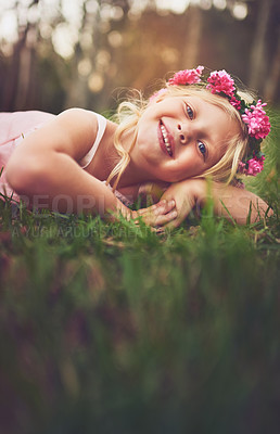 Buy stock photo Shot of a happy little girl looking at the camera while lying on the ground outside in nature