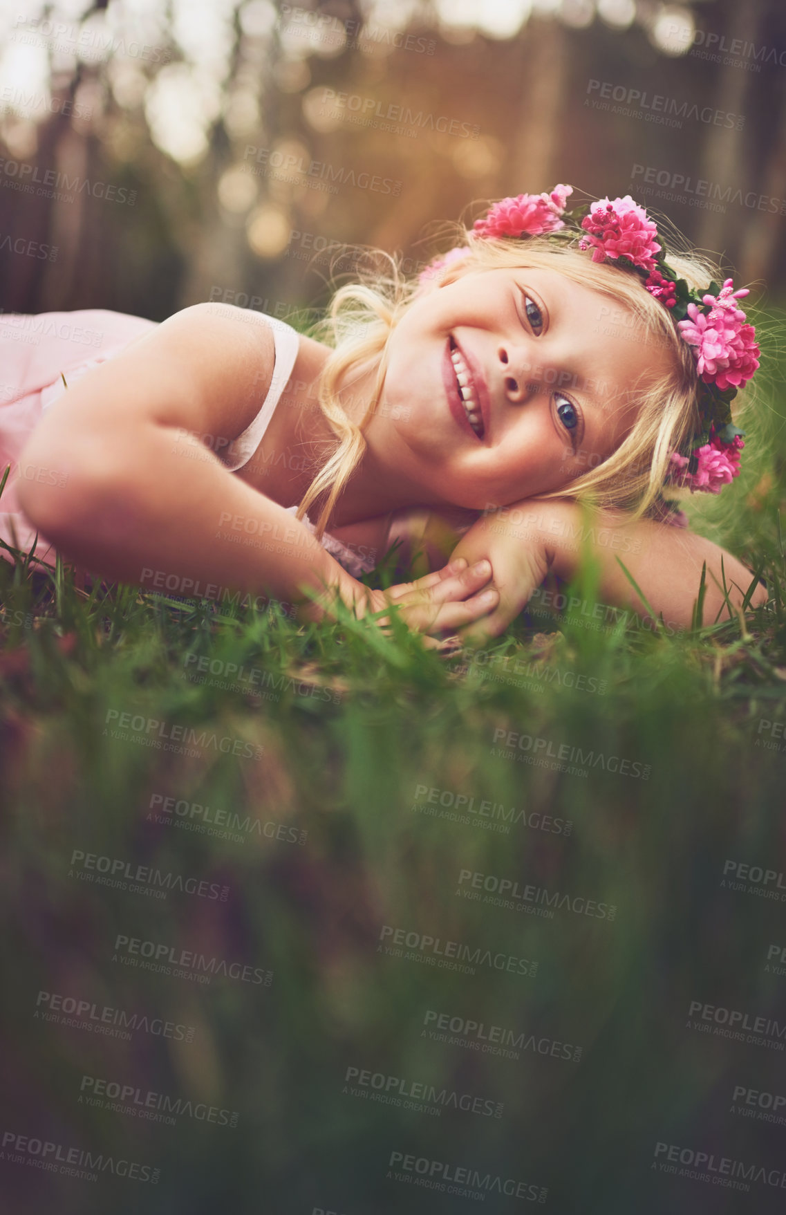 Buy stock photo Shot of a happy little girl looking at the camera while lying on the ground outside in nature