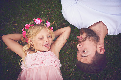 Buy stock photo Shot of a happy daughter and father lying on the ground sticking their tongues out at each other outside in nature